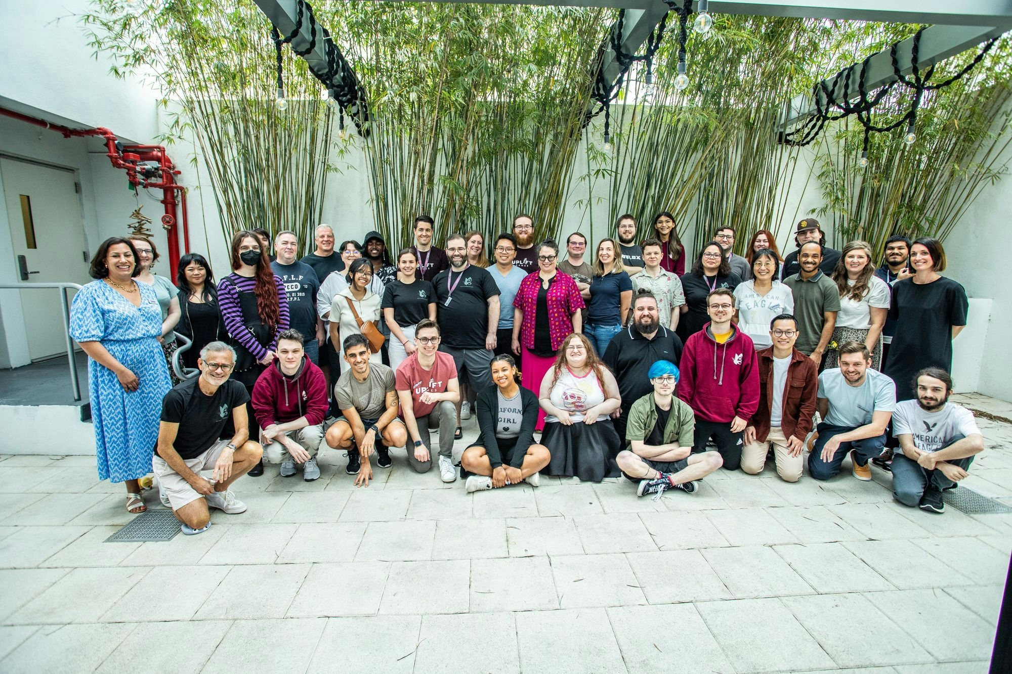 A group photo of Team Uplift at the Uplift Conference 2023. 43 people standing and kneeling for a group photo in a courtyard surrounded by green bamboo plants, everyone is smiling.. 