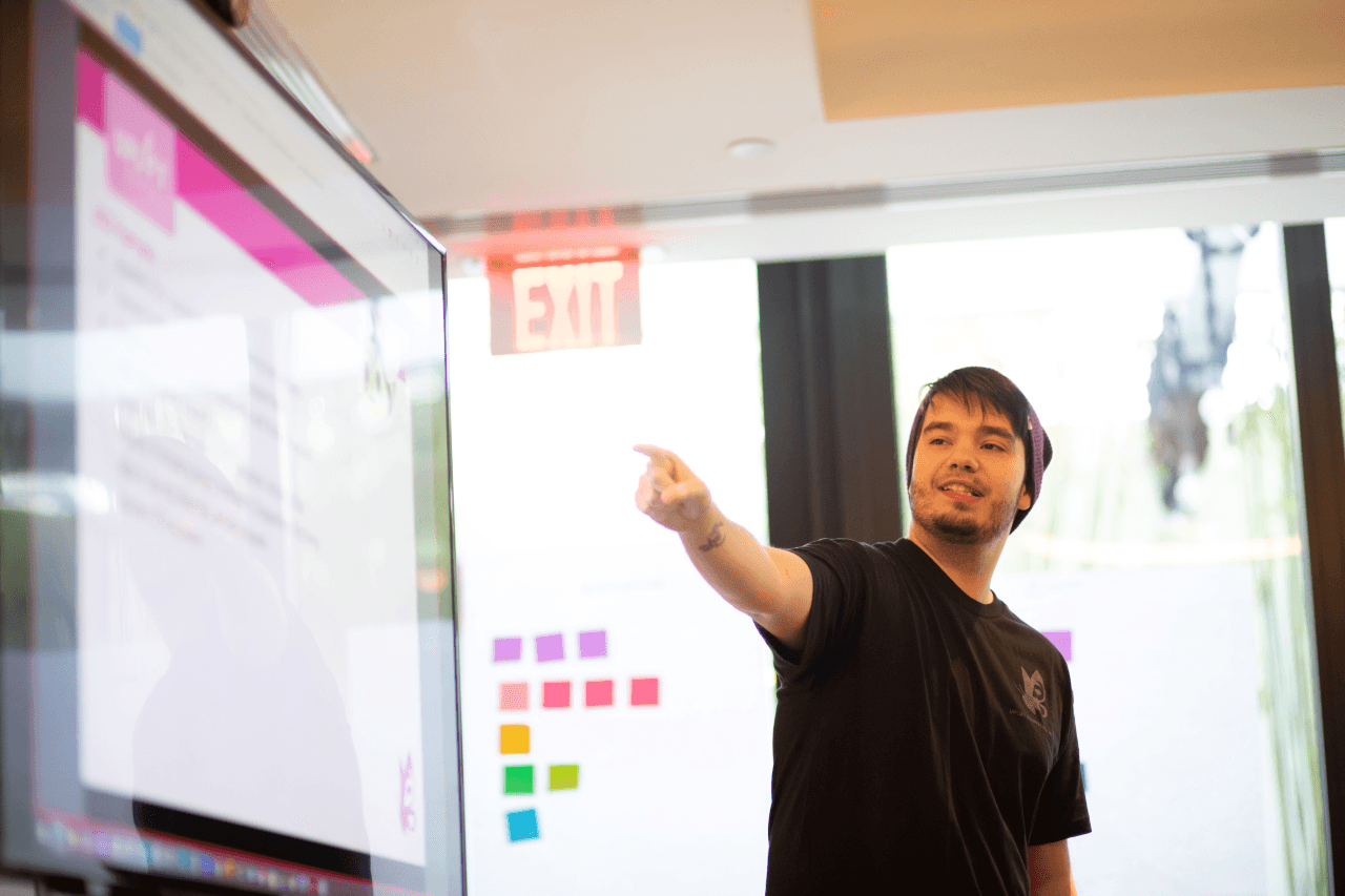 A Uplift Games employee pointing at a whiteboard of sticky notes.